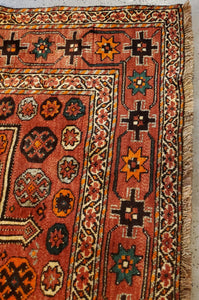 corner view of a Hand-Knotted Qashqai Rug, it has cinnamon fringe, white borders and light paprika colored main border with geometric patterns