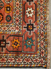Load image into Gallery viewer, Corner view of a Hand-Knotted Qashqai Rug, it has cinnamon fringe, white borders and light paprika colored main border with geometric patterns